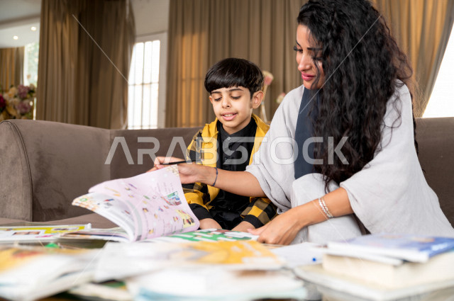 A Saudi Gulf student studying at home with his mother, helping him to do his homework, distance learning, the concept of online education, home education during quarantine and the outbreak of the Corona virus, self-isolation.