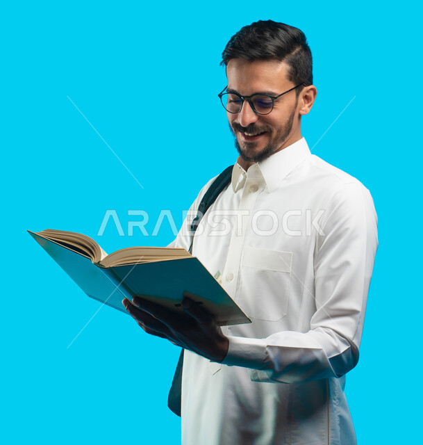 إيماءات وجه ويدين تدل على الفرح والسعادة ، التعليم الجامعي في المملكة العربية السعودية ، تدوين الملاحظات وكتابة تقارير وأبحاث علمية ، بورتريه لطالب جامعي عربي سعودي يرتدي الزي الخليجي و يحمل بيده كتب ، مراجعة الدروس اليومية ، خلفية زرقاء