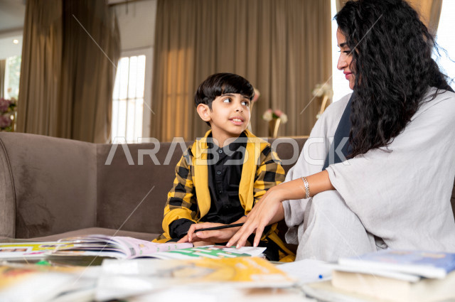 تلميذ سعودي خليجي يدرس في المنزل مع والدته ، تساعده على تأدية واجباته المدرسية ، التعلم عن بعد ، مفهوم التعليم عبر الانترنت ، التعليم المنزلي اثناء الحجر الصحي و تفشي فيروس كورونا ، العزلة الذاتية .