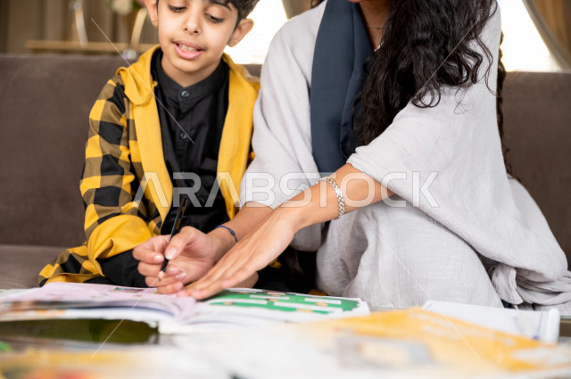 تلميذ سعودي خليجي يدرس في المنزل مع والدته ، تساعده على تأدية واجباته المدرسية ، التعلم عن بعد ، مفهوم التعليم عبر الانترنت ، التعليم المنزلي اثناء الحجر الصحي و تفشي فيروس كورونا ، العزلة الذاتية .