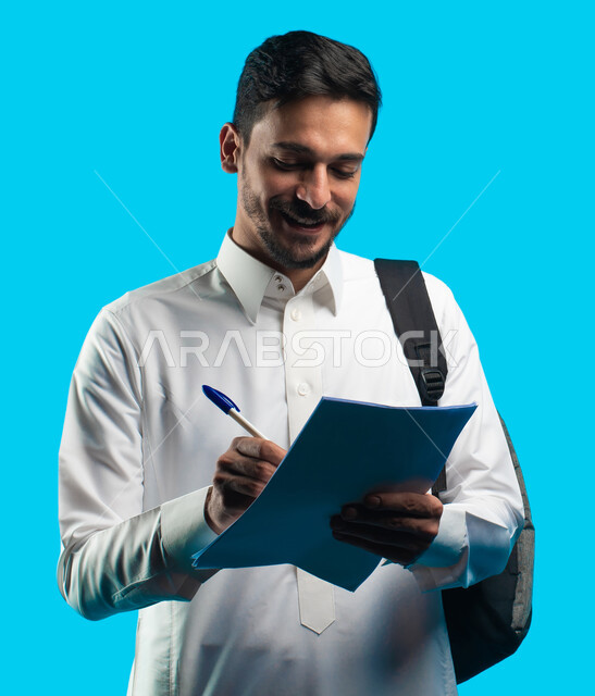 مراجعة الدروس اليومية ،  تدوين الملاحظات وكتابة تقارير أبحاث علمية ، إيماءات تدل على السعادة بإجتياز الإمتحان ، بورتريه لطالب جامعي عربي يرتدي الزي الخليجي السعودي و يحمل بيده أوراق الإختبار ، التعليم الجامعي في المملكة العربية السعودية ، خلفية زرقاء