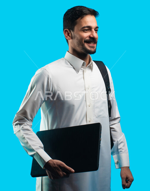 Education in the Kingdom of Saudi Arabia, gestures indicating happiness and joy in passing the exam, the use of modern technical devices, a portrait of an Arab university student wearing the Saudi Gulf uniform and holding a laptop in his hand, preparation