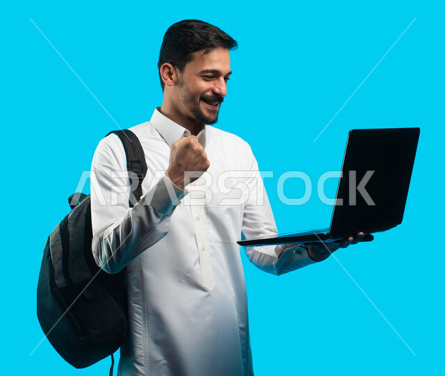 إيماءات تدل على السعادة والفرح ، إستخدام أجهزه تقنية حديثة ،  بورتريه لطالب جامعي عربي يرتدي الزي الخليجي السعودي ويقوم بإجراء مكالمة فيديو من خلال كمبيوتر محمول ، الإستعداد للمحاضرات الالكترونية ، التعلم عن بعد ، مراجعة الدروس اليومية ، خلفية زرقاء 
