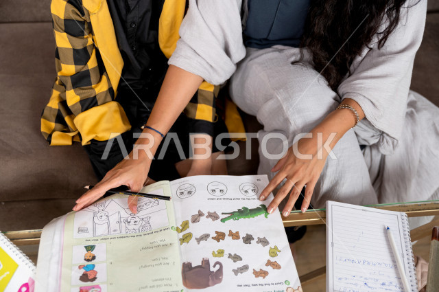 تلميذ سعودي خليجي يدرس في المنزل مع والدته ، تساعده على تأدية واجباته المدرسية ، التعلم عن بعد ، مفهوم التعليم عبر الانترنت ، التعليم المنزلي اثناء الحجر الصحي و تفشي فيروس كورونا ، العزلة الذاتية .