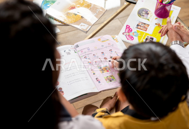 تلميذ سعودي خليجي يدرس في المنزل مع والدته ، تساعده على تأدية واجباته المدرسية ، التعلم عن بعد ، مفهوم التعليم عبر الانترنت ، التعليم المنزلي اثناء الحجر الصحي و تفشي فيروس كورونا ، العزلة الذاتية .