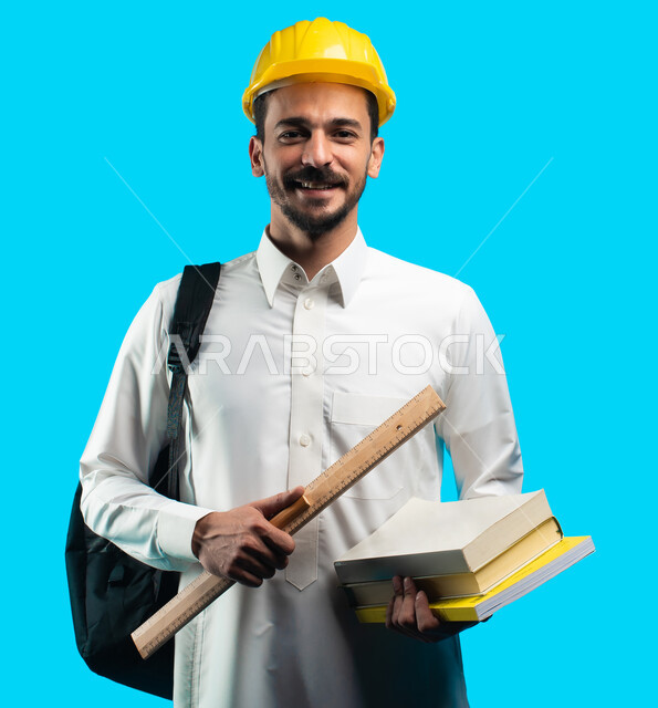 Engineering project management, education in the Kingdom of Saudi Arabia, facial gestures indicating joy and success, a portrait of a university student wearing the Saudi Gulf uniform holding engineering books and equipment in his hand, taking notes and w