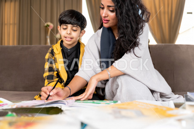 تلميذ سعودي خليجي يدرس في المنزل مع والدته ، تساعده على تأدية واجباته المدرسية ، التعلم عن بعد ، مفهوم التعليم عبر الانترنت ، التعليم المنزلي اثناء الحجر الصحي و تفشي فيروس كورونا ، العزلة الذاتية .