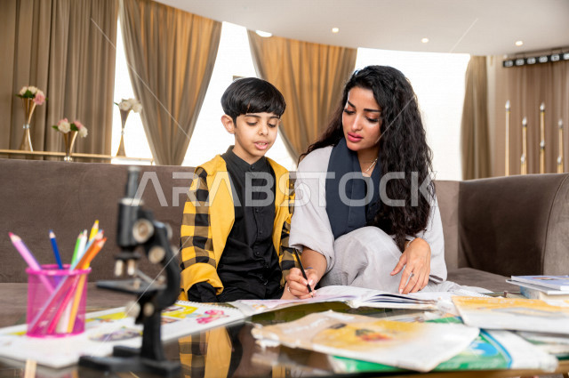 تلميذ سعودي خليجي يدرس في المنزل مع والدته ، تساعده على تأدية واجباته المدرسية ، التعلم عن بعد ، مفهوم التعليم عبر الانترنت ، التعليم المنزلي اثناء الحجر الصحي و تفشي فيروس كورونا ، العزلة الذاتية .