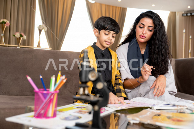 تلميذ سعودي خليجي يدرس في المنزل مع والدته ، تساعده على تأدية واجباته المدرسية ، التعلم عن بعد ، مفهوم التعليم عبر الانترنت ، التعليم المنزلي اثناء الحجر الصحي و تفشي فيروس كورونا ، العزلة الذاتية .