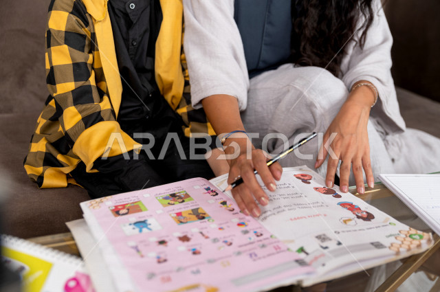 A Saudi Gulf student studying at home with his mother, helping him to do his homework, distance learning, the concept of online education, home education during quarantine and the outbreak of the Corona virus, self-isolation.