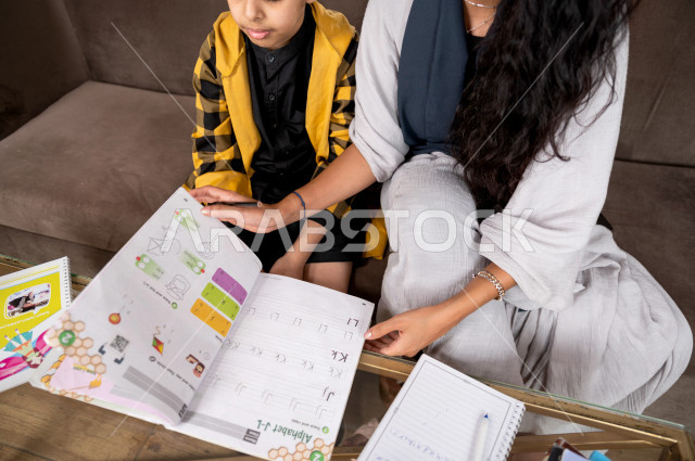A Saudi Gulf student studying at home with his mother, helping him to do his homework, distance learning, the concept of online education, home education during quarantine and the outbreak of the Corona virus, self-isolation.