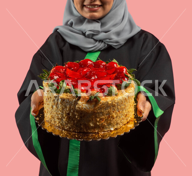 Happy festive atmosphere, a female graduate holding a cake mold decorated with fruits, a portrait of a Saudi Arabian Gulf university student wearing a gown and graduation cap, success, excellence and graduation from the university, education in the Kingdo