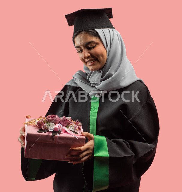 A happy festive atmosphere, facial gestures indicating happiness, a portrait of a Saudi Arabian Gulf university graduate wearing an abaya and a graduation hat and holding a gift box in her hand, success, excellence and graduation from the university, educ