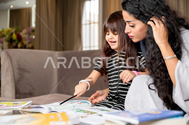 تلميذة سعودية خليجية تدرس في المنزل مع والدتها ، تساعدها على تأدية واجباتها المدرسية ، التعلم عن بعد ، مفهوم التعليم عبر الانترنت ، التعليم المنزلي اثناء الحجر الصحي و تفشي فيروس كورونا ، العزلة الذاتية .