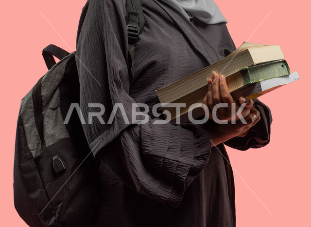 قراءة الكتب ومراجعة الدروس اليومية، الإستعداد للعام الدراسي الجامعي الجديد، بورتريه مقرب لطالبة جامعية عربية سعودية خليجية تحمل الكتب وحقيبة ظهر، التعليم في المملكة العربية السعودية، خلفية وردية