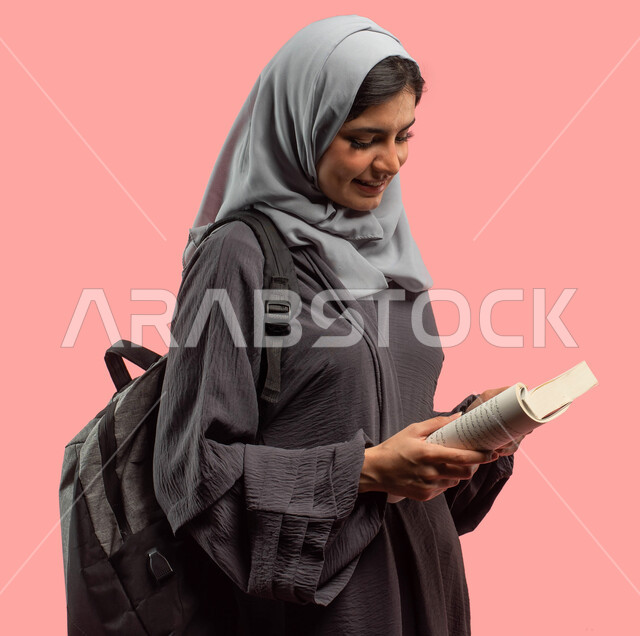 قراءة الكتب ومراجعة الدروس اليومية، بورتريه لطالبة جامعية عربية سعودية خليجية تمسك الكتاب وتحمل حقيبة الظهر، الإستعداد للعام الدراسي الجامعي الجديد، التعليم في المملكة العربية السعودية، إيماءات وجه تدل على السعادة، خلفية وردية