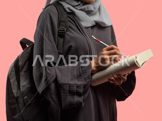 تدوين الملاحظات وكتابة التقارير والأبحاث العلمية، بورتريه مقرب لطالبة جامعية عربية سعودية خليجية تحمل حقيبة ظهر وتمسك كتاب، الإستعداد للعام الدراسي الجامعي الجديد، قراءة ومراجعة الدروس اليومية، التعليم في المملكة العربية السعودية، خلفية وردية