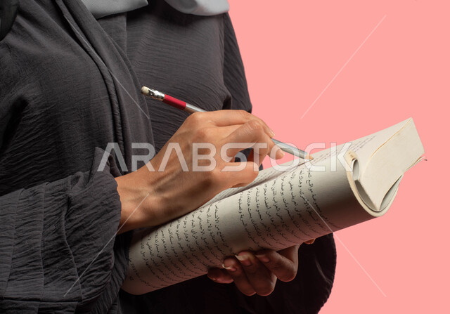 Close-up portrait of a female Saudi Arabian Gulf university student holding a book and taking notes and writing reports and scientific research, preparing for the new academic year, reading and reviewing daily lessons, education in the Kingdom of Saudi Ar