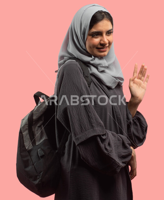 التلويح باليد لإلقاء التحية والترحيب، بورتريه لطالبة جامعية عربية سعودية خليجية تحمل حقيبة ظهر، الإستعداد للعام الدراسي الجامعي الجديد، التعليم في المملكة العربية السعودية، إيماءات يدين تدل على السلام، خلفية وردية