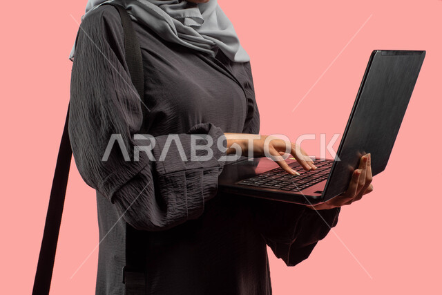التعليم الإلكتروني والتعلم عن بعد، بورتريه مقرب لإمرأة عربية خليجية تحمل بيدها جهاز الحاسوب المحمول، إنجاز مهام العمل وتصفح الانترنت، إحتراف وظائف الحاسوب وتكنولوجيا المعلومات، خلفية وردية