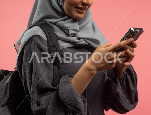 تصفح التطبيقات ووسائل التواصل الاجتماعي، بورتريه مقرب لطالبة جامعية عربية خليجية سعودية تحمل حقيبة الظهر وتستخدم الهاتف المحمول، البحث والمطالعة من خلال الجوال، الاستعداد للعام الدراسي الجامعي الجديد، خلفية وردية