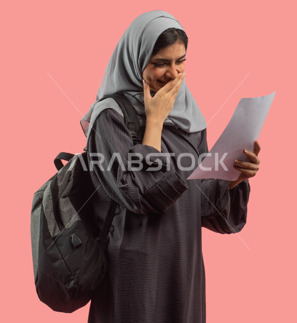Success in the university exam and passing the academic stage, a portrait of a Saudi Arab Gulf university student carrying a backpack and holding the test paper, face and hands gestures indicating joy and happiness, education in the Kingdom of Saudi Arabi