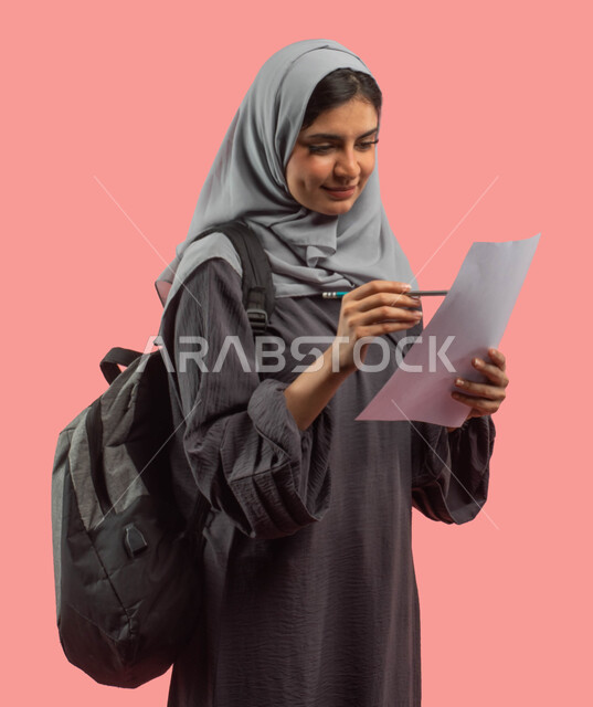 قراءة ومراجعة الدروس اليومية، بورتريه لطالبة عربية سعودية خليجية تمسك ورقة وقلم وتحمل حقيبة ظهر، تدوين الملاحظات وكتابة التقارير والأبحاث العلمية، التعليم في المملكة العربية السعودية، الإستعداد للعام الدراسي الجديد، خلفية وردية
