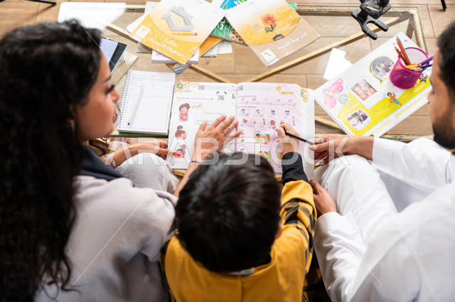 تلميذ سعودي خليجي يدرس في المنزل مع والده و والدته ، يساعدانه على تأدية واجباته المدرسية ، التعلم عن بعد ، مفهوم التعليم عبر الانترنت ، التعليم المنزلي اثناء الحجر الصحي و تفشي فيروس كورونا ، العزلة الذاتية .