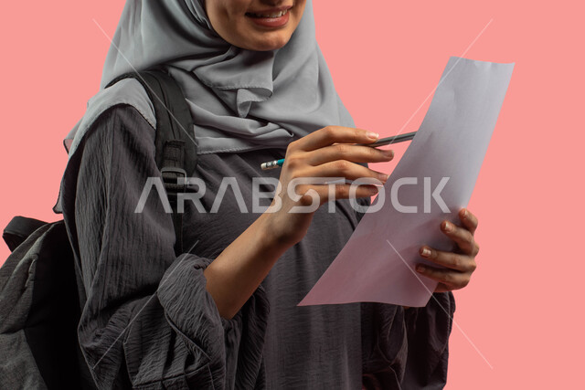تدوين الملاحظات وكتابة التقارير والأبحاث العلمية، بورتريه مقرب لطالبة عربية سعودية خليجية تمسك ورقة وقلم وتحمل حقيبة ظهر، قراءة ومراجعة الدروس اليومية، التعليم في المملكة العربية السعودية، الإستعداد للعام الدراسي الجديد، خلفية وردية