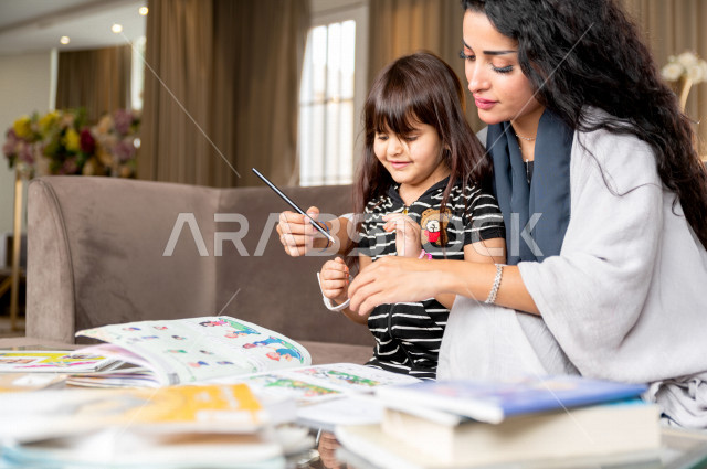 تلميذة سعودية خليجية تدرس في المنزل مع والدتها ، تساعدها على تأدية واجباتها المدرسية ، التعلم عن بعد ، مفهوم التعليم عبر الانترنت ، التعليم المنزلي اثناء الحجر الصحي و تفشي فيروس كورونا ، العزلة الذاتية .