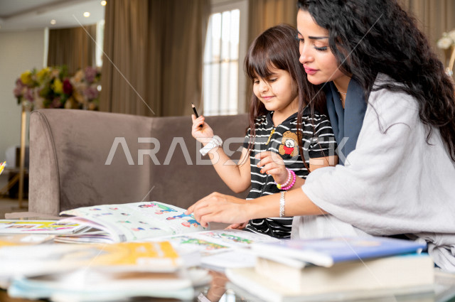 تلميذة سعودية خليجية تدرس في المنزل مع والدتها ، تساعدها على تأدية واجباتها المدرسية ، التعلم عن بعد ، مفهوم التعليم عبر الانترنت ، التعليم المنزلي اثناء الحجر الصحي و تفشي فيروس كورونا ، العزلة الذاتية .