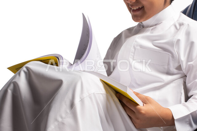  قضاء الوقت بالقراءة والتعلم والتثقف، ايماءات وتعابير وجه تدل على الاستمتاع بالمطالعة، بورتريه لصبي عربي سعودي خليجي يرتدي الزي السعودي يجلس على كرسي مريح ويحمل بيديه كتاب  ، الاستمتاع بقراءة الكتب , ثقافة التعليم الذاتي, خلفية بيضاء