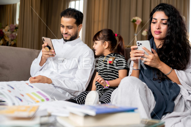 تلميذة سعودية خليجية تدرس في المنزل مع والدها و والدتها ، يساعدانها على تأدية واجباتها المدرسية ، استخدام الهاتف المحمول لمتابعة التعليم ، مفهوم التعليم عبر الانترنت ، التعليم المنزلي اثناء الحجر الصحي و تفشي فيروس كورونا ، العزلة الذاتية .