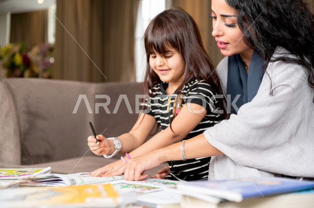 تلميذة سعودية خليجية تدرس في المنزل مع والدتها ، تساعدها على تأدية واجباتها المدرسية ، التعلم عن بعد ، مفهوم التعليم عبر الانترنت ، التعليم المنزلي اثناء الحجر الصحي و تفشي فيروس كورونا ، العزلة الذاتية .