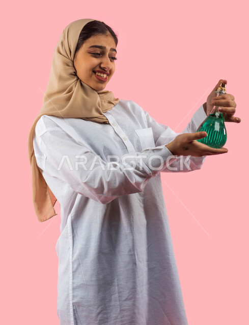 مفهوم الأناقة والاهتمام بالمظهر الخارجي، التسويق لمنتجات العطور، بورتريه لامرأة عربية سعودية خليجية تقوم بحمل زجاجة عطر، استخدام الزيوت العطرية الطبيعية،  استخدام مستحضرات نسائية لمزيد من الجمال والأناقة، صورة مقربة لفتاة بخلفية زهرية