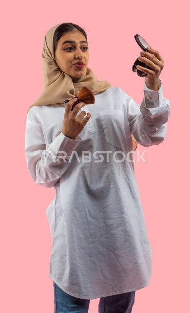  أدوات تجميل نسائيه عصريه، التسويق لمنتجات التجميل, بورتريه لفتاه عربيه سعودية خليجيه تحمل بيدها مستحضرات توريد الخدود, مفهوم الانوثه والاهتمام بالمظهر الخارجي, مكياج وميكاب تتوريال, صالون نسائي راقي, خلفيه ورديه. 