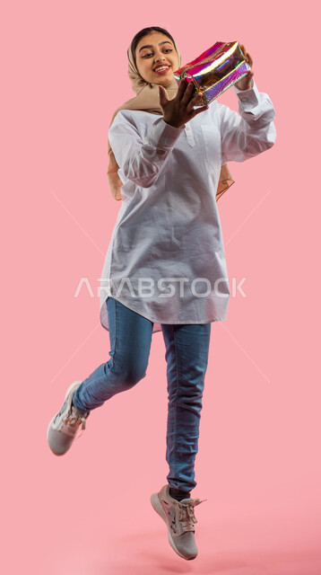 Shopping from malls and bag stores, a portrait of a Saudi Arabian Gulf girl holding a shiny makeup bag in her hand, jumping gestures and happiness with the pleasure of buying and owning gifts, a small elegant party bag, modern women's fashion and accessor