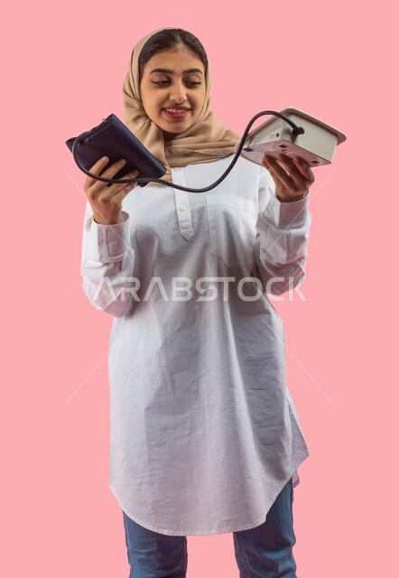 التسويق للأجهزه والأدوات الطبيه الحديثه, جهاز قياس ضغط الدم الالكتروني, بورتريه لشابه عربيه سعوديه خليجيه تستخدم جهاز الضغط, التسوق والشراء من محلات ومتاجر القطاع الطبي والصحي, خلفيه ورديه. 