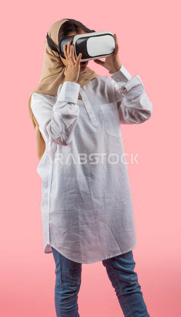  الاستمتاع والاندماج مع مشاهدة العالم الافتراضي العصري الحديث, مشاهدة أفلام ثلاثية الابعاد عبر نظارة الواقع الافتراضي, فتاه عربيه سعوديه خليجيه ترتدي الزي الكاجوال ونظارات العالم الخيالي , التطور التقني والتكنولوجي , تسليه وترفيه, خلفيه ورديه. 