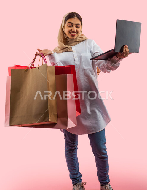 Enjoying buying and selling online, White Friday offers and discounts, facial gestures indicating enjoyment of shopping and buying gifts, a portrait of a Saudi Arab Gulf woman wearing casual clothes carrying bags in her hand, safe electronic shopping, hom