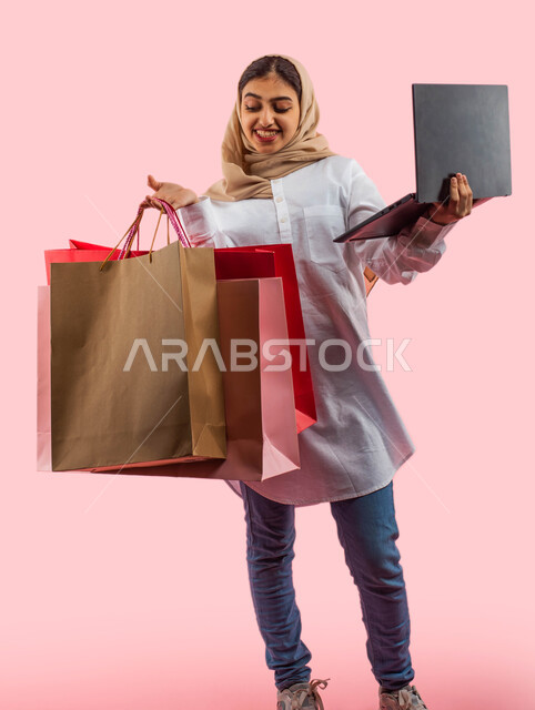 الشراء والبيع عبر الاونلاين، عروض وتخفيضات الجمعة البيضاء، ايماءات وجه تدل على الإستمتاع بالتسوق و شراء الهدايا، بورتريه لإمرأة عربية سعودية خليجية ترتدي الزي الكاجوال تحمل بيدها أكياس، التسوق الإلكتروني الآمن ، خدمة التوصيل إلى المنازل ، خلفية وردية.