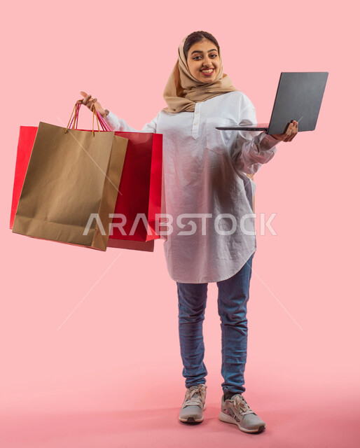 White Friday offers and discounts, facial gestures indicating enjoyment of shopping and buying gifts, a portrait of a Saudi Arabian Gulf woman in casual attire carrying bags in her hand, safe electronic shopping, online purchase, full-length body image, p