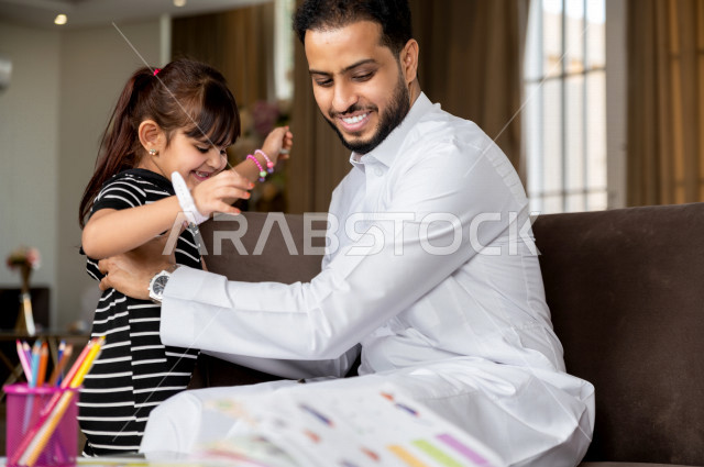 طفلة سعودية خليجية تلعب مع والدها بعد الانتهاء من حل الواجبات المدرسية ، التعلم عن بعد ، مفهوم التعليم عبر الانترنت ، التعليم المنزلي اثناء الحجر الصحي و تفشي فيروس كورونا ، العزلة الذاتية .