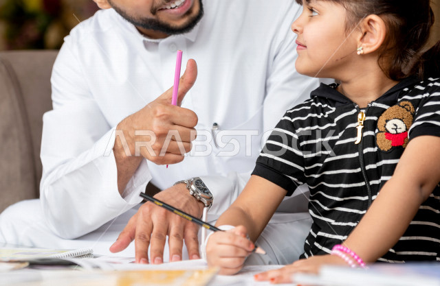 تلميذة سعودية خليجية تدرس في المنزل مع والدها ، يساعدها على تأدية واجباتها المدرسية ، التعلم عن بعد ، مفهوم التعليم عبر الانترنت ، التعليم المنزلي اثناء الحجر الصحي و تفشي فيروس كورونا ، العزلة الذاتية .