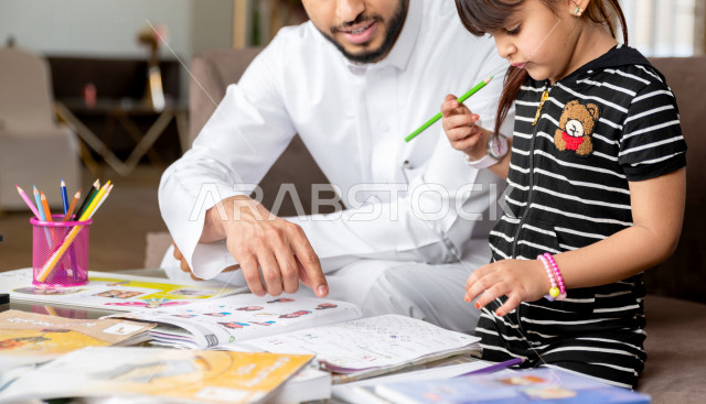 تلميذة سعودية خليجية تدرس في المنزل مع والدها ، يساعدها على تأدية واجباتها المدرسية ، التعلم عن بعد ، مفهوم التعليم عبر الانترنت ، التعليم المنزلي اثناء الحجر الصحي و تفشي فيروس كورونا ، العزلة الذاتية .