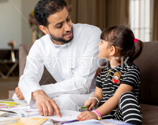 تلميذة سعودية خليجية تدرس في المنزل مع والدها ، يساعدها على تأدية واجباتها المدرسية ، التعلم عن بعد ، مفهوم التعليم عبر الانترنت ، التعليم المنزلي اثناء الحجر الصحي و تفشي فيروس كورونا ، العزلة الذاتية .