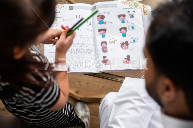 تلميذة سعودية خليجية تدرس في المنزل مع والدها ، يساعدها على تأدية واجباتها المدرسية ، التعلم عن بعد ، مفهوم التعليم عبر الانترنت ، التعليم المنزلي اثناء الحجر الصحي و تفشي فيروس كورونا ، العزلة الذاتية .