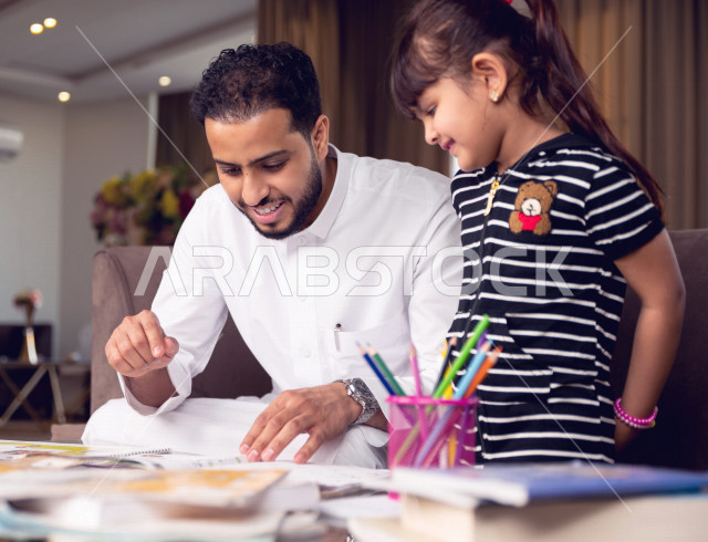 تلميذة سعودية خليجية تدرس في المنزل مع والدها ، يساعدها على تأدية واجباتها المدرسية ، التعلم عن بعد ، مفهوم التعليم عبر الانترنت ، التعليم المنزلي اثناء الحجر الصحي و تفشي فيروس كورونا ، العزلة الذاتية .