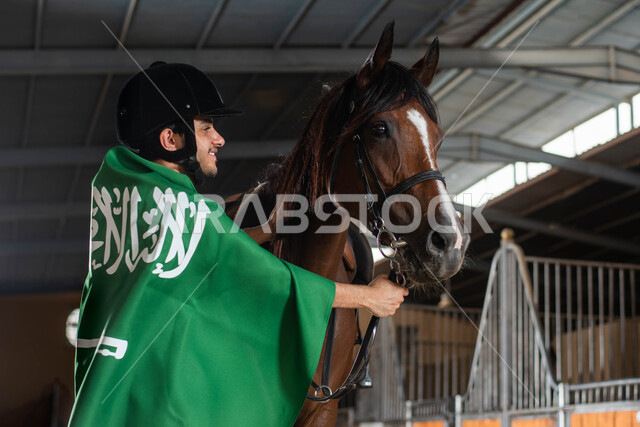 الاحتفال باليوم الوطني السعودي , فرس بني عربي أصيل , رعاية وتدريب وترويض الأحصنة , أنشطة ترفيهية في اسطبل الخيول , هواية ركوب الخيل, مدرب أحصنة عربي سعودي خليجي يرتدي علم السعودية على ظهره   , ذكرى يوم التأسيس, يوم العلم السعودي