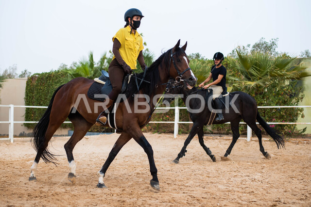 قضاء أوقات ممتعة برفقة الأصدقاء،نادي الفروسية في المملكة العربية السعودية، شاب و شابة عربيان خليجيان سعوديان يمتطيان الخيول العربية الأصيلة, إرتداء زي الفروسيه, أنشطة ترفيهية وفعاليات رياضية مع الأحصنة،  الإلتزام بالاحترازات الوقائية بإرتداء الكمامة.